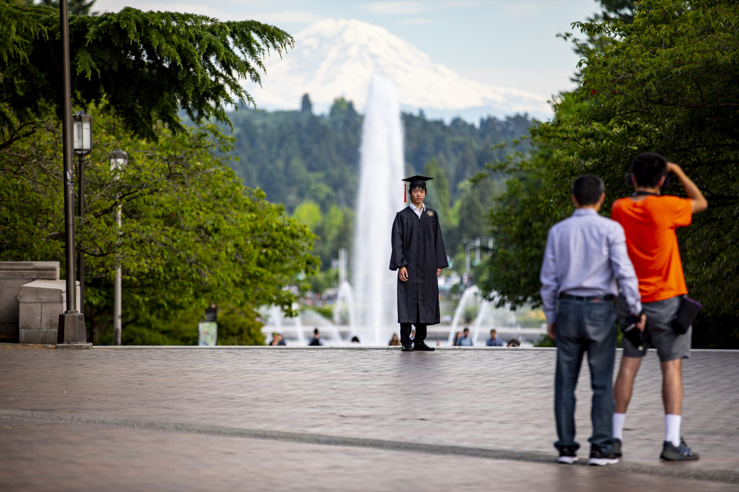 Graduate posing near Drumheller Fountain with Mount Rainier in the distance
