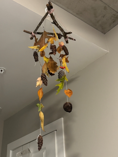 A chandelier made of twigs, leaves, and pinecones hangs from a ceiling